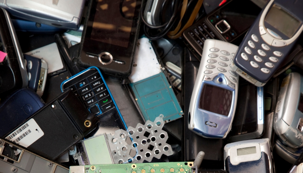 including vintage cell phones and computer chips are piled in a recycling bin.