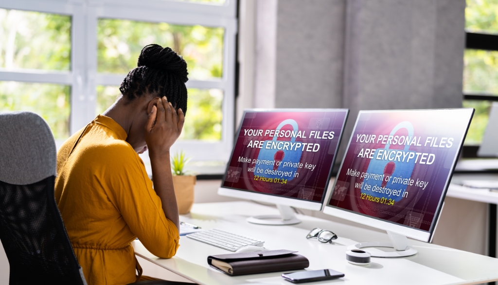 Distresses employee working from home with computer displaying encrypted files error message.|Woman working from home with computers displaying a data breach warning.