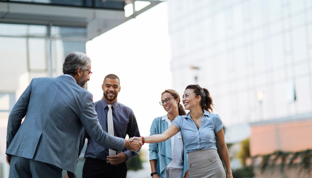 Business partners demonstrating service excellence while shaking hands outside of an office building.|Business partners shaking hands outside of an office building.