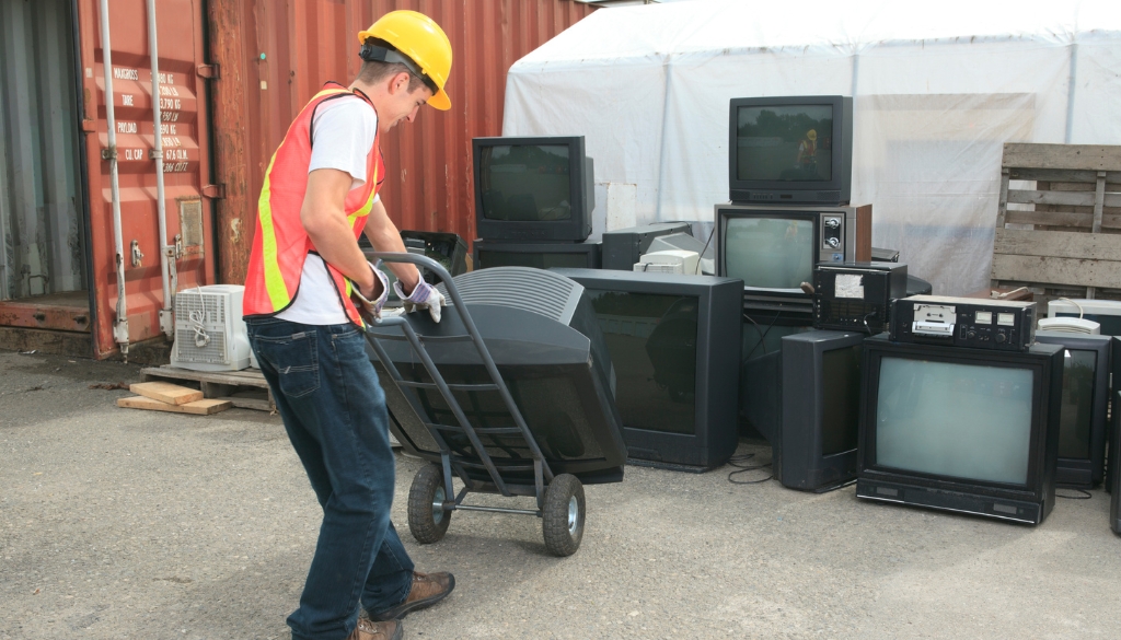 Worker moving TVs on a dolly to be recycled.|TV with grass on the screen.